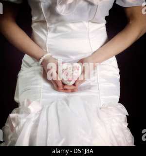eine Frau in einem weißen Kleid mit einem floralen Herzen in ihren Händen Stockfoto
