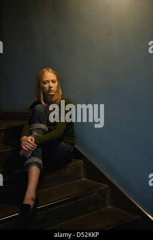 Junge Frau sitzt auf der Treppe, umarmt Knie Stockfoto