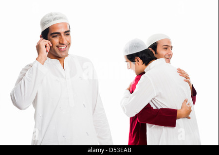 Mann sprechen auf einem Handy mit seinen Freunden umarmen einander während der Eid festival Stockfoto