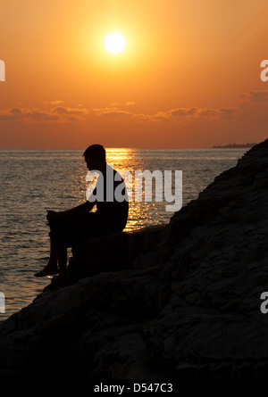 Silhouette des Menschen von der Seite auf einem Felsen sitzen und den Sonnenuntergang genießen Stockfoto