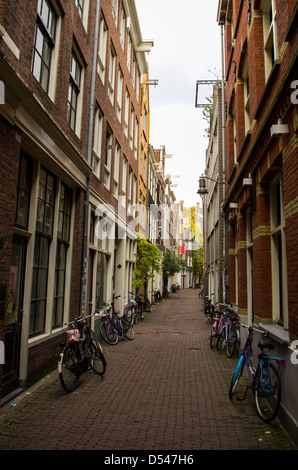 Eine schmale Straße in Amsterdam mit dem Fahrrad geparkt entlang der Häuser. vertikale Stockfoto