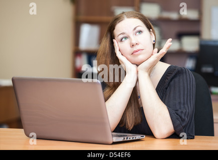 Nachdenkliche Frau eine Brünette denken sitzen am Schreibtisch mit Laptop im Büro Stockfoto