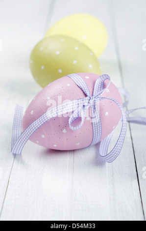 Mehrfarbig bemalte Ostereier mit violett karierte Schleife auf weißem Holz Hintergrund Stockfoto