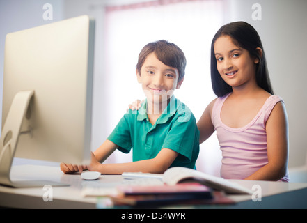 Porträt von zwei Kindern, die lächelnd an einen Schreibtisch Stockfoto