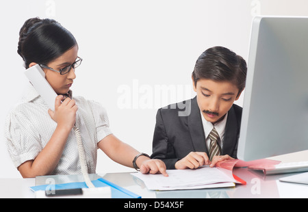 Junge imitieren wie Geschäftsmann Prüfung Unterlagen mit einem Mädchen imitieren wie seine Sekretärin eine Festnetz telefonieren Stockfoto