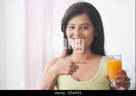 Glückliche Frau zeigt auf ein Glas Orangensaft Stockfoto