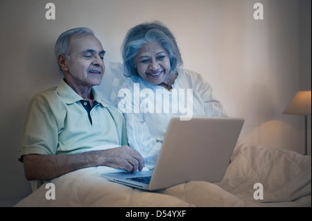 Älteres Paar mit einem Laptop auf dem Bett und lächelnd Stockfoto