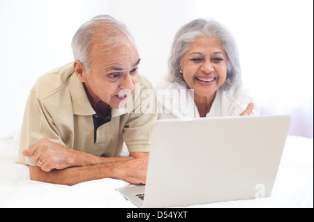 Älteres Paar mit einem Laptop auf dem Bett und lächelnd Stockfoto