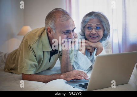 Älteres Paar mit einem Laptop auf dem Bett und lächelnd Stockfoto