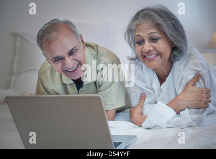 Älteres Paar mit einem Laptop auf dem Bett und lächelnd Stockfoto