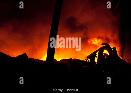 Silhouette der Feuerwehrleute kämpfen ein wütendes Feuer mit riesigen Flammen des brennenden Holzes Stockfoto