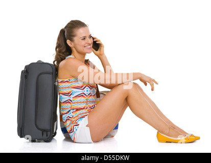 Glückliche junge Touristen Frau sitzt in der Nähe von Laufradtasche und Handy im Gespräch Stockfoto