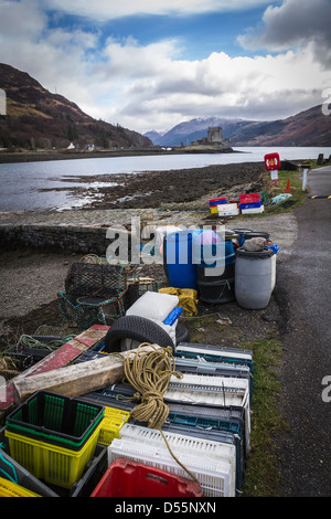 Plastikfische Container und Hummer Töpfe am Ufer des Loch Duich, Eilean Donan Castle im Hintergrund in leuchtenden Farben. Stockfoto