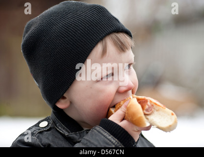 Kleiner Junge Essen einen Hotdog im freien Blick zur Seite Stockfoto