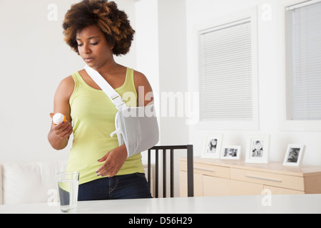 Afroamerikanische Frau in Schlinge, die Einnahme von Medikamenten Stockfoto