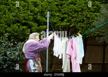 Ältere Frau, die gewaschene Wäsche für die natürliche Trocknung im Garten an einem windigen Tag hängen Stockfoto