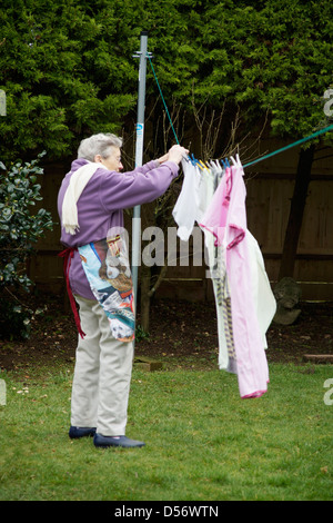 Ältere Frau, die gewaschene Wäsche für die natürliche Trocknung im Garten an einem windigen Tag hängen Stockfoto