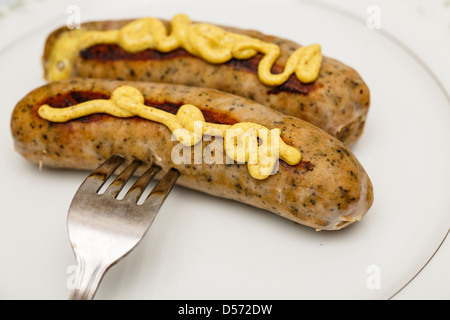 Zwei Würste auf einem weißen Teller mit einer Gabel mit würzigen Senf Stockfoto