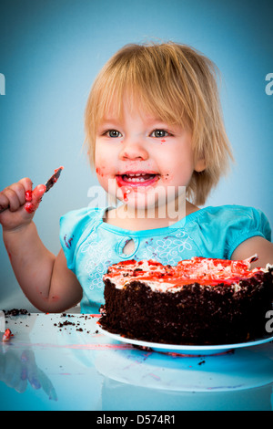 Kleines Mädchen essen Kuchen auf blauem Hintergrund Stockfoto