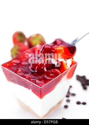 Käsekuchen mit Kirschen und Erdbeer-Gelee in eine Glasschüssel dekoriert von Erdbeeren und Schokolade-chips Stockfoto