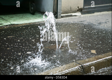 Ein Hahn auf dem Bürgersteig ist fehlgeschlagen, verursacht einen kleinen Brunnen Wasser abperlen Stockfoto