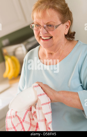 Lächelnd Senior Erwachsene Frau Trocknung Schüssel an Spüle in der Küche. Stockfoto