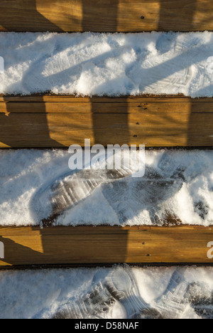 Licht und Schatten fallen gegen die horizontalen Streifen von Fußspuren auf verschneiten Holzstufen. Stockfoto