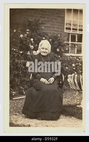 Postkarte von einer älteren Frau Edwardian sitzen vor ihrem Haus trägt eine Spitze Mütze, ca. 1905, U.K Stockfoto