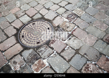 Runde Stahl Kanalisation Kanaldeckel auf gepflasterten Straße Stockfoto