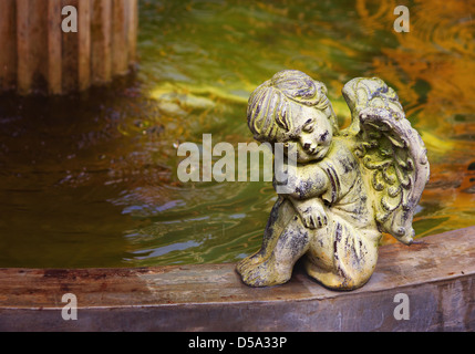 Cherub neben dem Brunnen. Niedliche kleine Engel-Statue aus Stein erbaut. Schöne warme Farben. Stockfoto