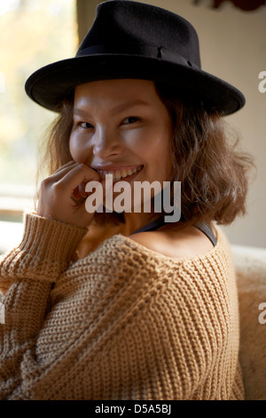 Schöne junge asiatische Modell mit schwarzem Hut und braunen Pullover zu Hause. Stockfoto