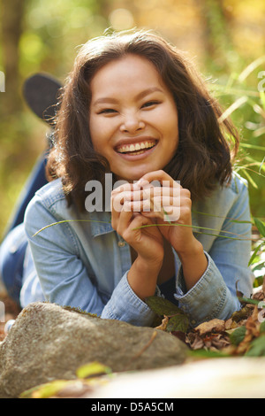 Schöne junge asiatische Modell tragen Jeanshemd Verlegung auf Boden in üppigem Grün an sonnigen Tag. Stockfoto