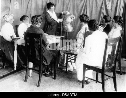 Dieses Foto zeigt eine Spezialistin für Erweiterungen, wahrscheinlich Bertha Titsworth, die eine Demonstration über die Verwendung einer Kleiderform für Hauswirtschaft oder Textilunterricht gibt. Das Bild ist Teil einer Serie, die sich mit den pädagogischen Praktiken des frühen 20. Jahrhunderts in Textilien befasst. Stockfoto