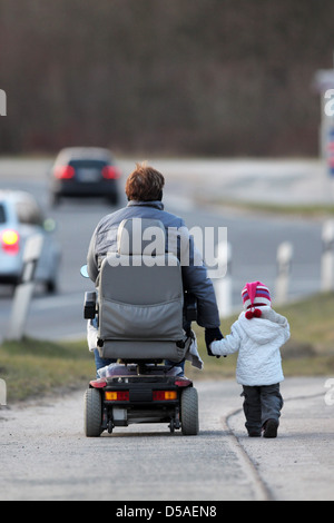 Handewitt, Deutschland, eine Großmutter laufen zu Fuß in einem elektrischen Rollstuhl mit ihrem Enkel Hand auf einem Fahrrad Stockfoto