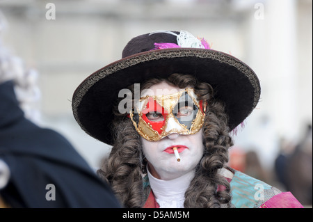 Ein maskierter Teilnehmer raucht eine Zigarette im Karneval in Venedig Stockfoto