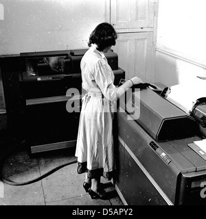 Historisches Bild aus den späten 1950er Jahren einer Frau, die in einem Büro mit einem Stück Rechnungswesen der Zeit, einem großen Datenprozessor und einer Druckmaschine arbeitet. Bekannt als "Tabulatoren", lasen sie Kartendecks und druckten ausgewählte Teile ihres Inhalts, addieren auch Zahlenkolonnen und drucken Summen. Komplexe und umständliche Maschinen, werden sie als die Vorläufer der frühen Computer. Stockfoto