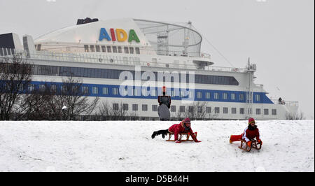 Kinder Rodeln während die 252m lange neu entwickelte Kreuzfahrtschiff, die "AIDAblu" aus der Meyer-Werft in Papenburg, Deutschland, im Hintergrund 5. Januar 2010 abgedockt werden wird. Der her von sechs Schiffe geplant, denn die AIDA Schiffseigner Firma in Rostock, Deutschland auf der EMS in die Nordsee transportiert werden soll. Foto: Carmen Jaspersen Stockfoto