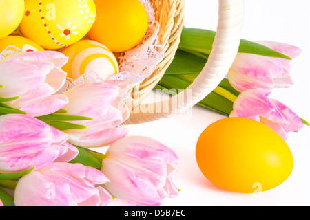 Ostern-Konzept. Korb, bemalte Ostereier und rosa Tulpen isoliert auf weißem Hintergrund. Stockfoto