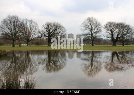 Richmond Park, England, Vereinigtes Königreich. 28. März 2013. Altem Baumbestand und die modernen Hochhäuser des Weingutes Alton spiegeln sich in den Teich, der sich gebildet hat, wo die endlose Regen Felder in der Nähe von Roehampton Gate in Richmond Park überflutet hat. Die größte der königlichen Parks, es ist eine nationale Natur-Reserve, Londons größte Site of Special Scientific Interest und einer europäischen Special Area of Conservation. Stockfoto