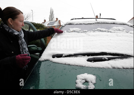 Eine Frau, die Schneeräumung von einem Auto Windschutzscheibe England uk Stockfoto