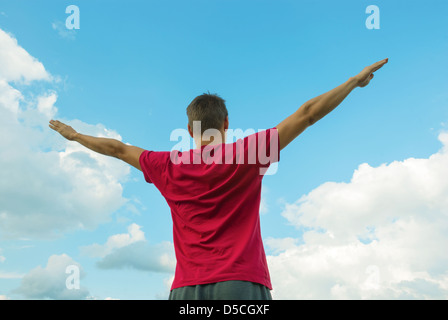 Junger Mann mit erhobenen Händen gegen blauen Himmel Stockfoto