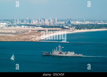 United States Navy Schiff betritt den Hafen von San Diego mit North Island Air Bahnhof und der Innenstadt von Gebäuden im Hintergrund Stockfoto