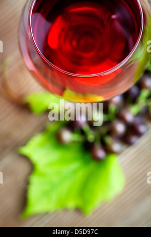 Glas Rotwein mit Trauben auf Tisch Stockfoto