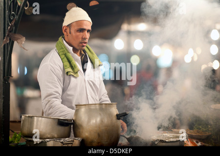 Ein Mann Kochen über einem rauchigen Feuer auf einem Wochenmarkt Stand in Djemaa al Fna Platz in Marrkesh, Marokko Stockfoto
