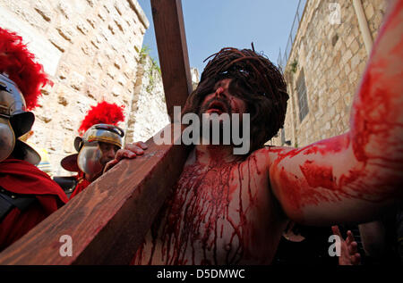 Ein Christ devotee gekleidet, wie Jesus Christus trägt ein hölzernes Kreuz reenacting die Stationen des Kreuzes während der Karfreitagsprozession entlang der Via Dolorosa Straße glaubte, daß der Weg zu sein, dass Jesus auf dem Weg zu seiner Kreuzigung in der Altstadt Ost Jerusalem, Israel ging Stockfoto