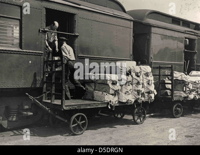 Ein Schwarzweißfoto, das 1925 Postsendungen auf einen Eisenbahnpostdienst (RPO) verladen hat. Dieses Bild zeigt die Effizienz des U.S. Railway Mail Service während seiner Spitzenphase und zeigt einen Kutschwagen, der für den Transport von Post durch das Land eingesetzt wird. Stockfoto