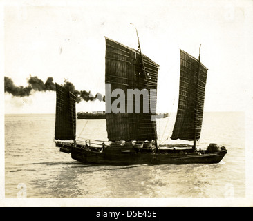 Ein chinesischer Dschunke wird mit einem Dampfschiff im Hintergrund gezeigt, das traditionelle chinesische Seeschiffe und moderne Dampfschifftechnologie widerspiegelt. Dieses Bild stellt den Kontrast zwischen Alt und Neu in der chinesischen maritimen Geschichte dar. Stockfoto