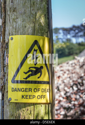 Eine gelbe "Lebensgefahr" 'Zu halten Off' Warnschild typische im Vereinigten Königreich. An einem hölzernen Strommast in der Landschaft genagelt. Stockfoto