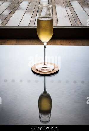 Ein einzelnes Sektglas sitzt auf einer hochglanzpolierten Tabelle, die die Reflexion zeigt. Stockfoto