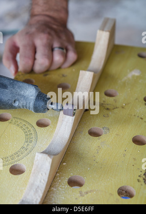 Nahaufnahme eines Mannes Schleifen Kurven, um eine glatte Oberfläche mit einem Dremel auf einem Brett aus Holz statt auf einer Werkbank, einem Weinregal zu machen. Stockfoto